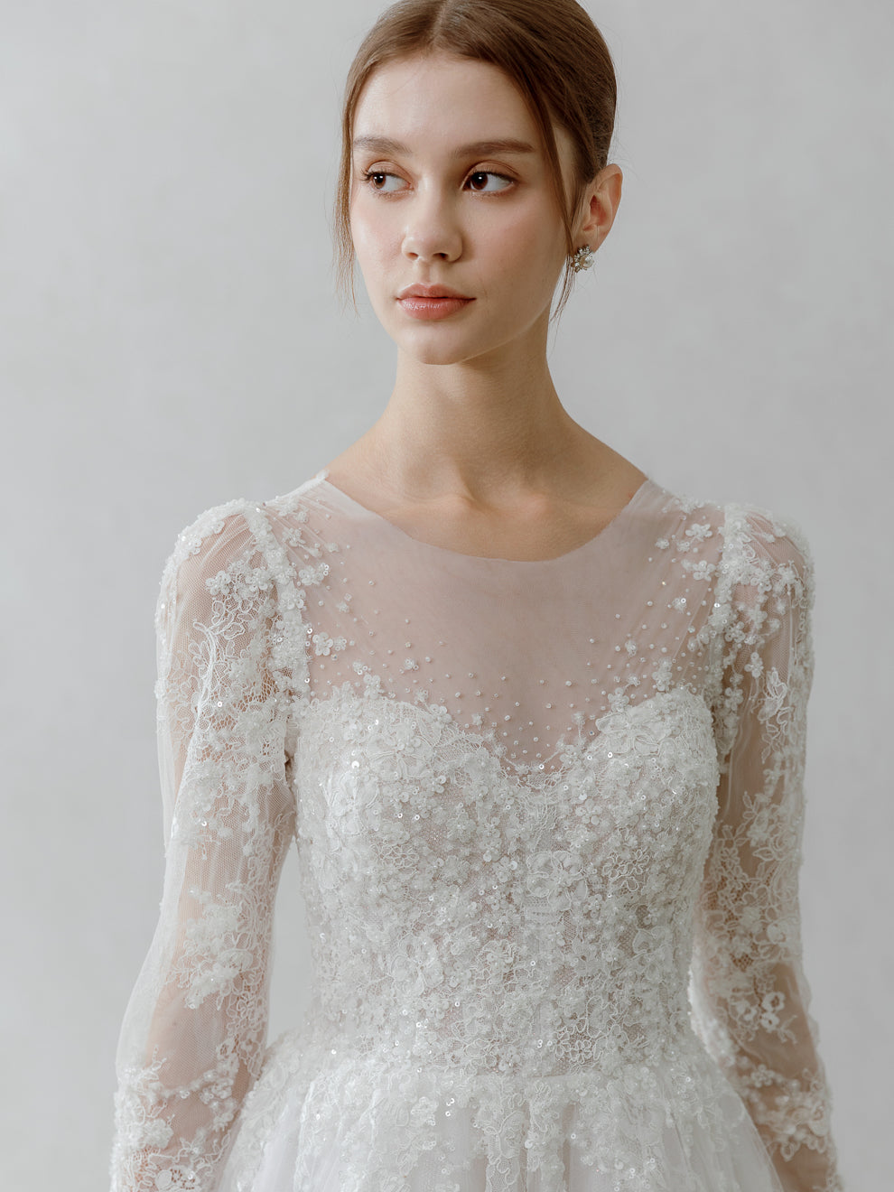 Woman wearing a white lace wedding dress against a plain background