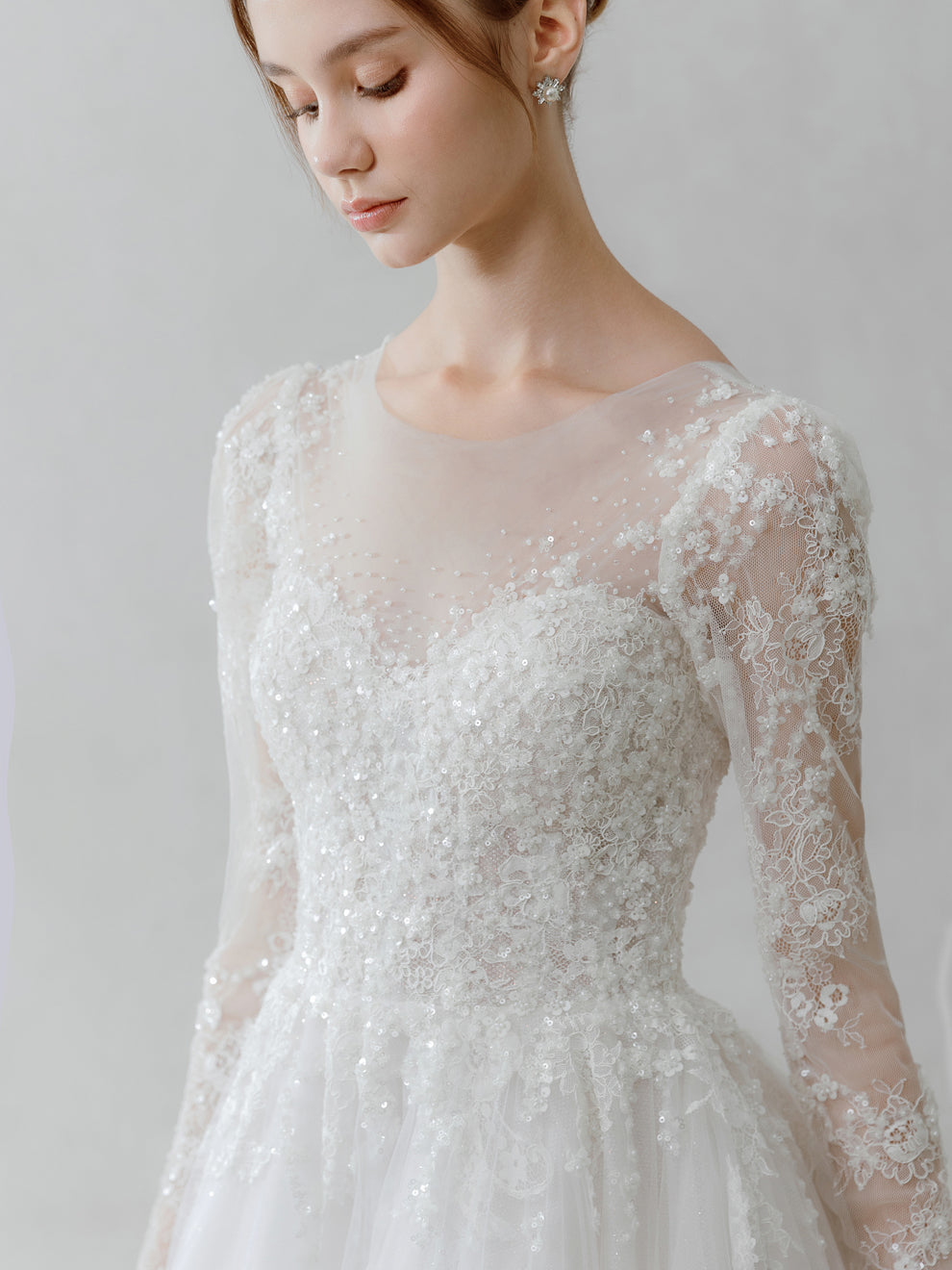 Woman wearing a lace wedding dress with long sleeves on a plain background