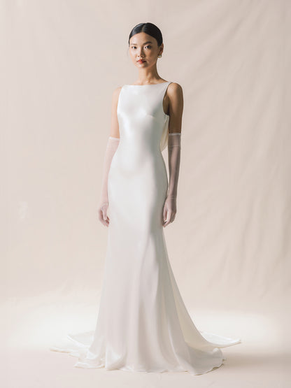 Woman wearing a white wedding dress with long gloves on a plain background