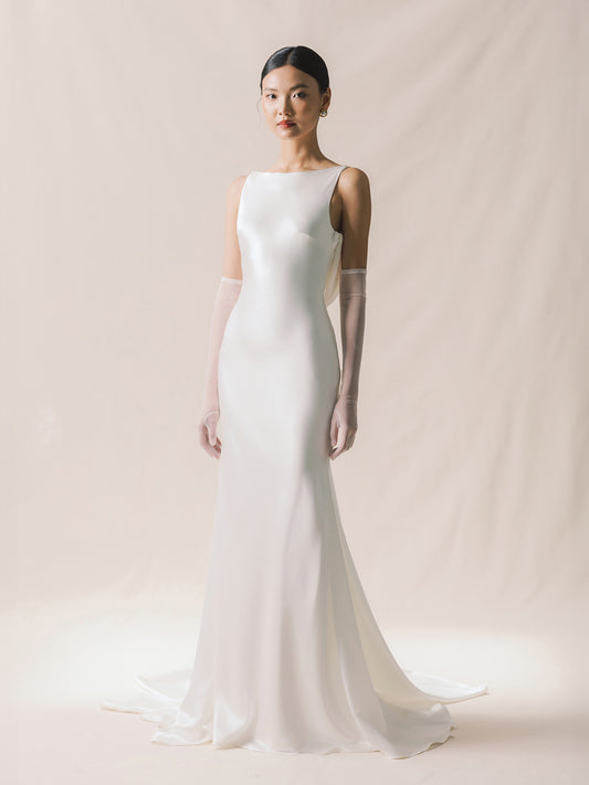 Woman wearing a white wedding dress with long gloves on a plain background