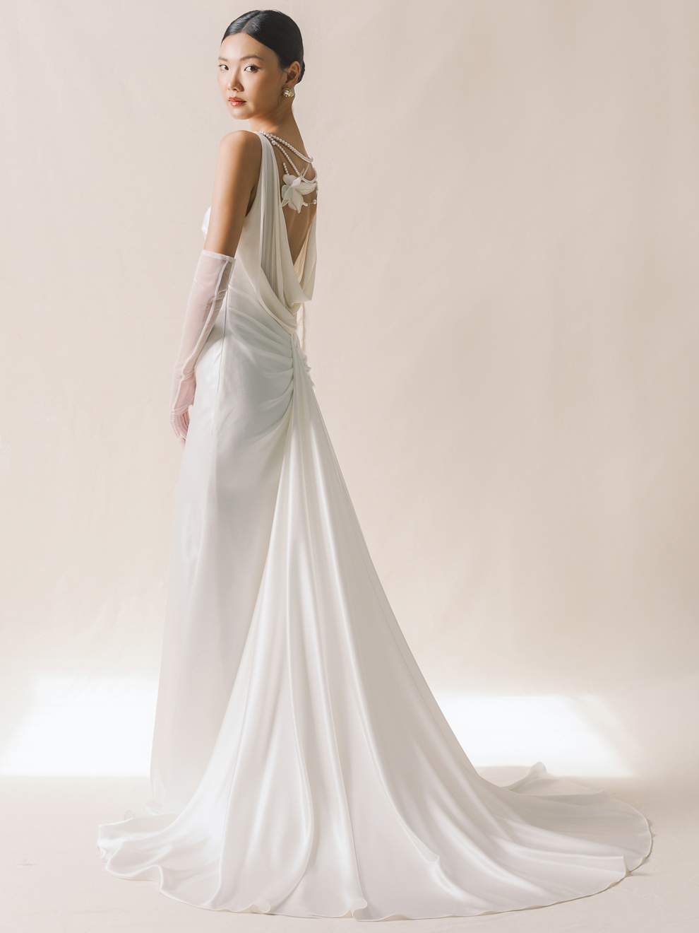 Woman wearing a white wedding dress with a long train against a plain background