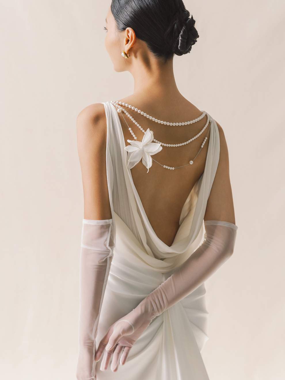 Woman in a wedding dress with a floral back detail and sheer sleeves on a plain background