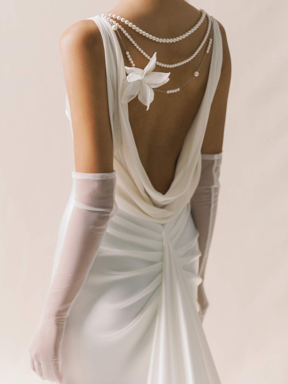 White wedding dress with open back, butterfly detail, and pearl necklace on a plain background