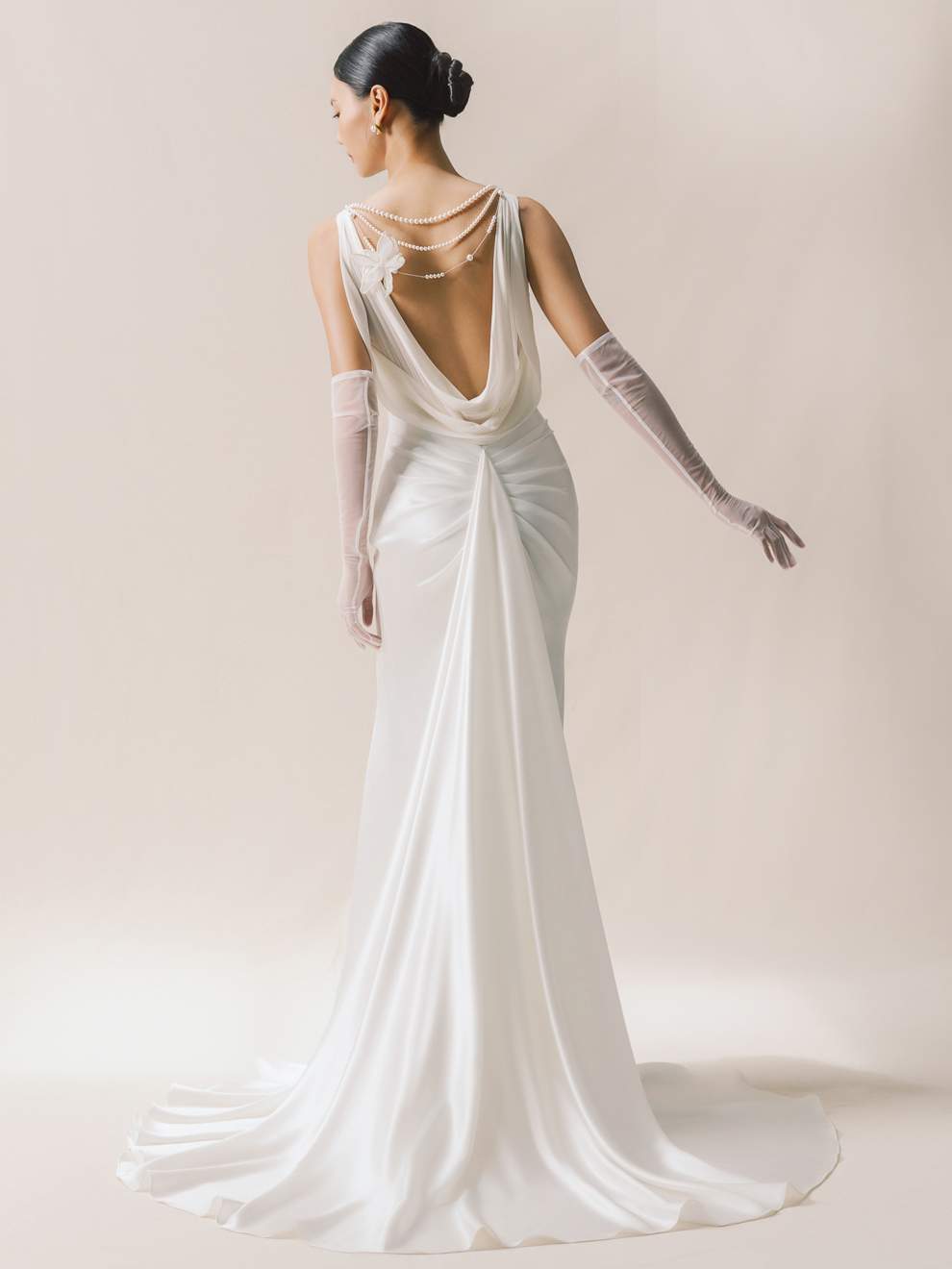 Woman wearing a white wedding dress with a low back and long gloves on a plain background