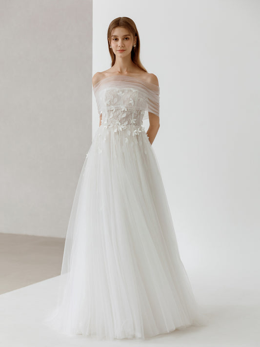 Woman wearing a white wedding dress with floral details against a plain background