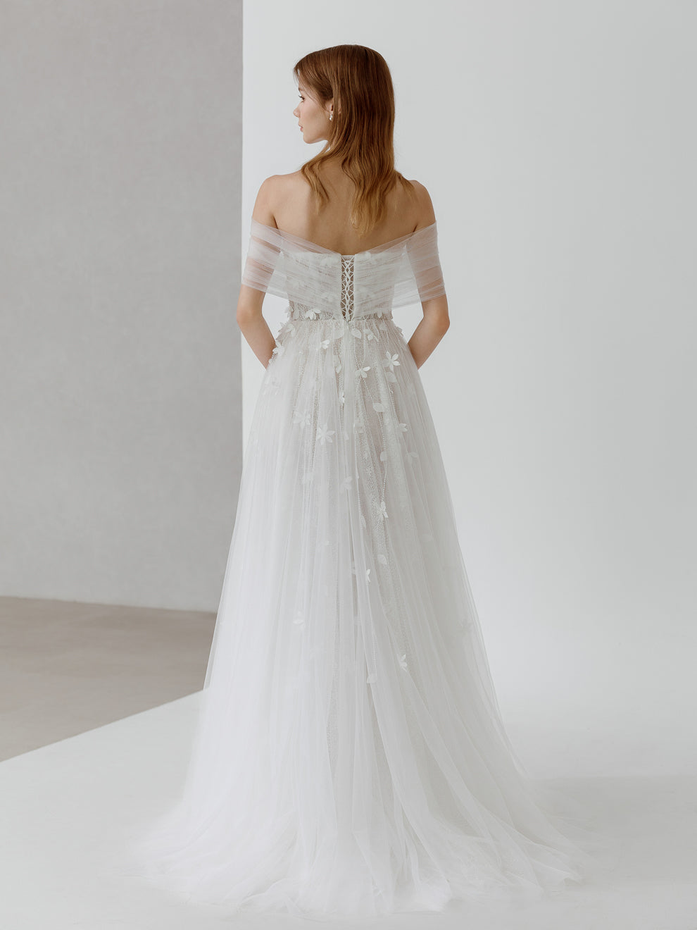 Woman wearing a white wedding dress with a subtle back design on a plain background
