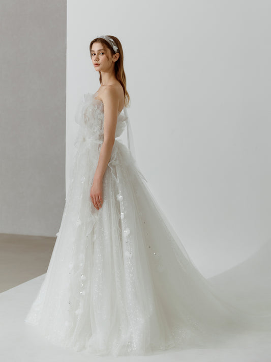 Woman wearing a white wedding dress with floral details against a plain background