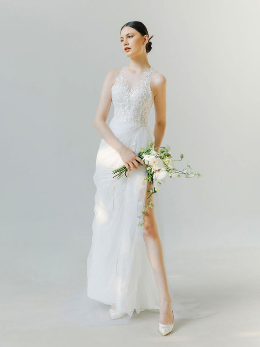 Woman in a white wedding dress holding a bouquet against a plain background