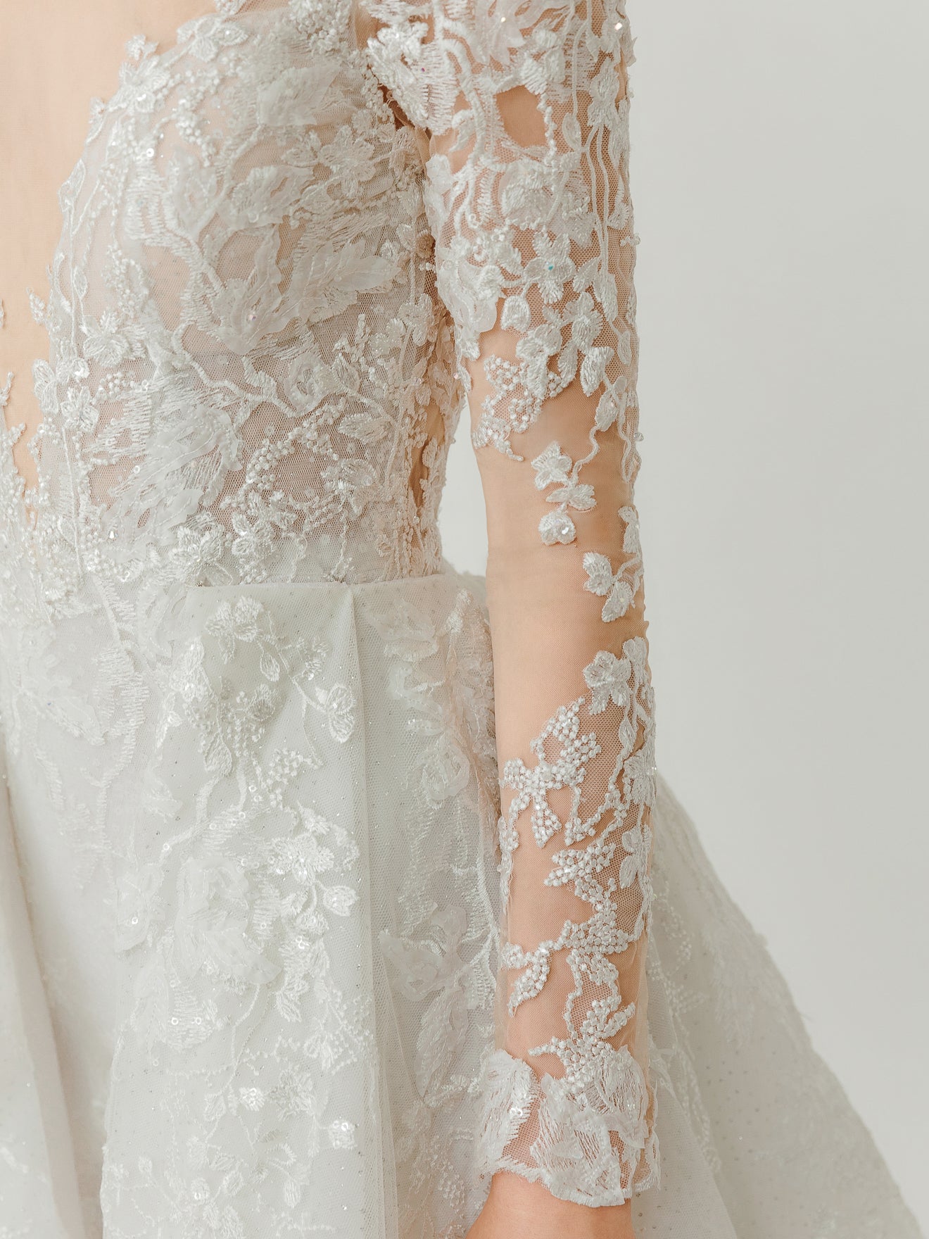Close-up of a white lace wedding dress with long sleeves on a plain background