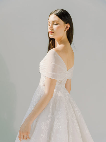 Woman wearing a light pink off-shoulder dress against a plain background