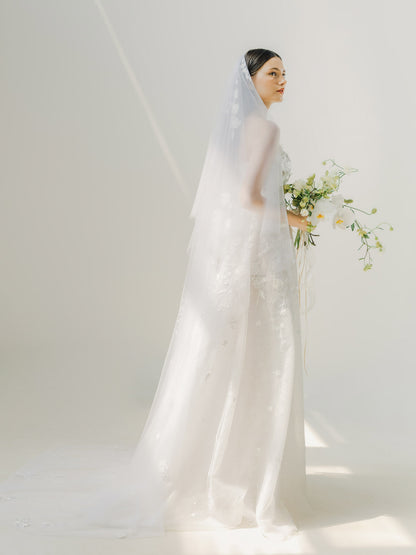 Woman in a white wedding dress holding flowers against a plain background