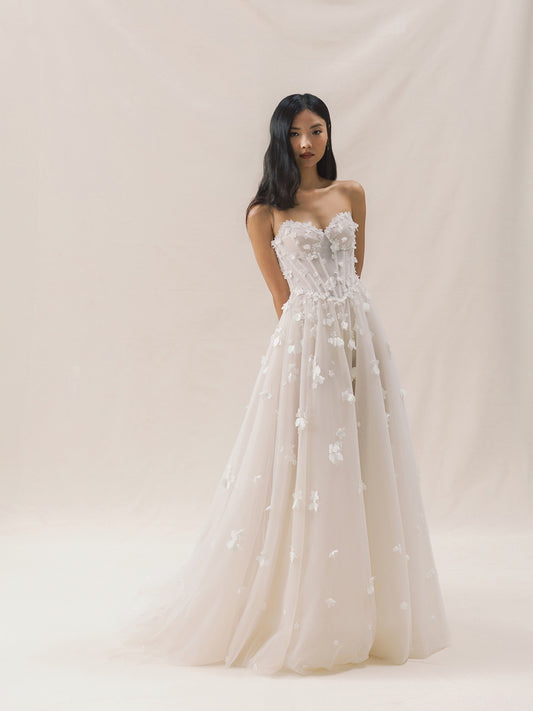 Woman wearing a strapless wedding dress with floral details on a plain background