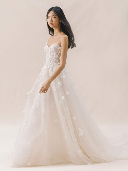 Woman wearing a strapless wedding dress with floral details against a plain background