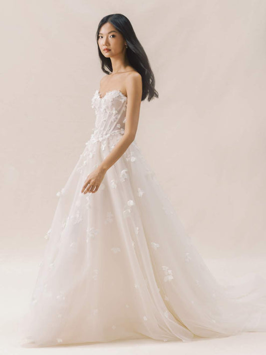 Woman wearing a strapless wedding dress with floral details against a plain background