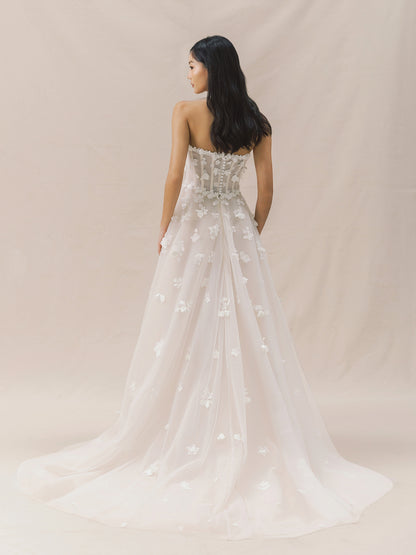 Woman wearing a strapless wedding dress with floral details on a beige background