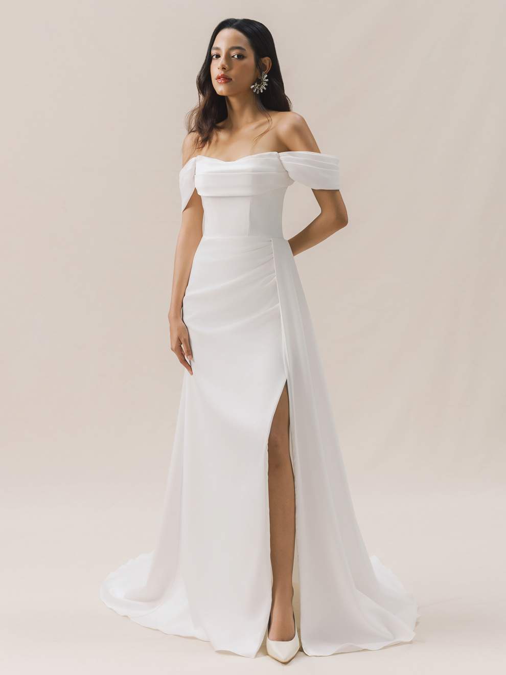 Woman wearing a white off-shoulder gown with a high slit on a plain background