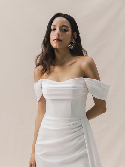 Woman wearing a white off-shoulder dress against a beige background