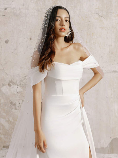Woman wearing a white off-shoulder wedding dress with a veil against a light background