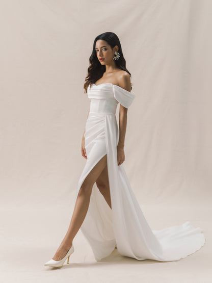 Woman wearing a white off-shoulder gown with a slit on a beige background