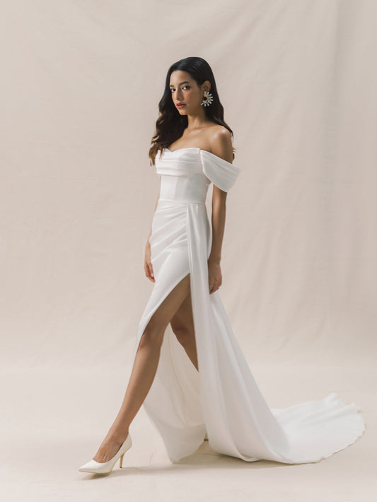 Woman wearing a white off-shoulder gown with a slit on a beige background