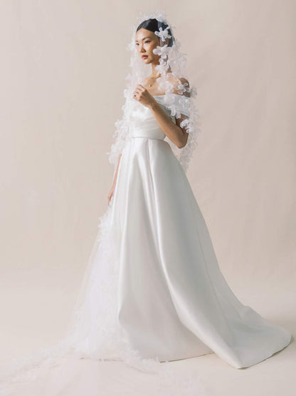Woman wearing a white wedding dress with a long train and floral headpiece on a plain background