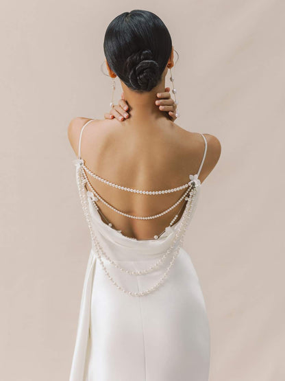 Woman wearing a white dress with pearl straps against a beige background