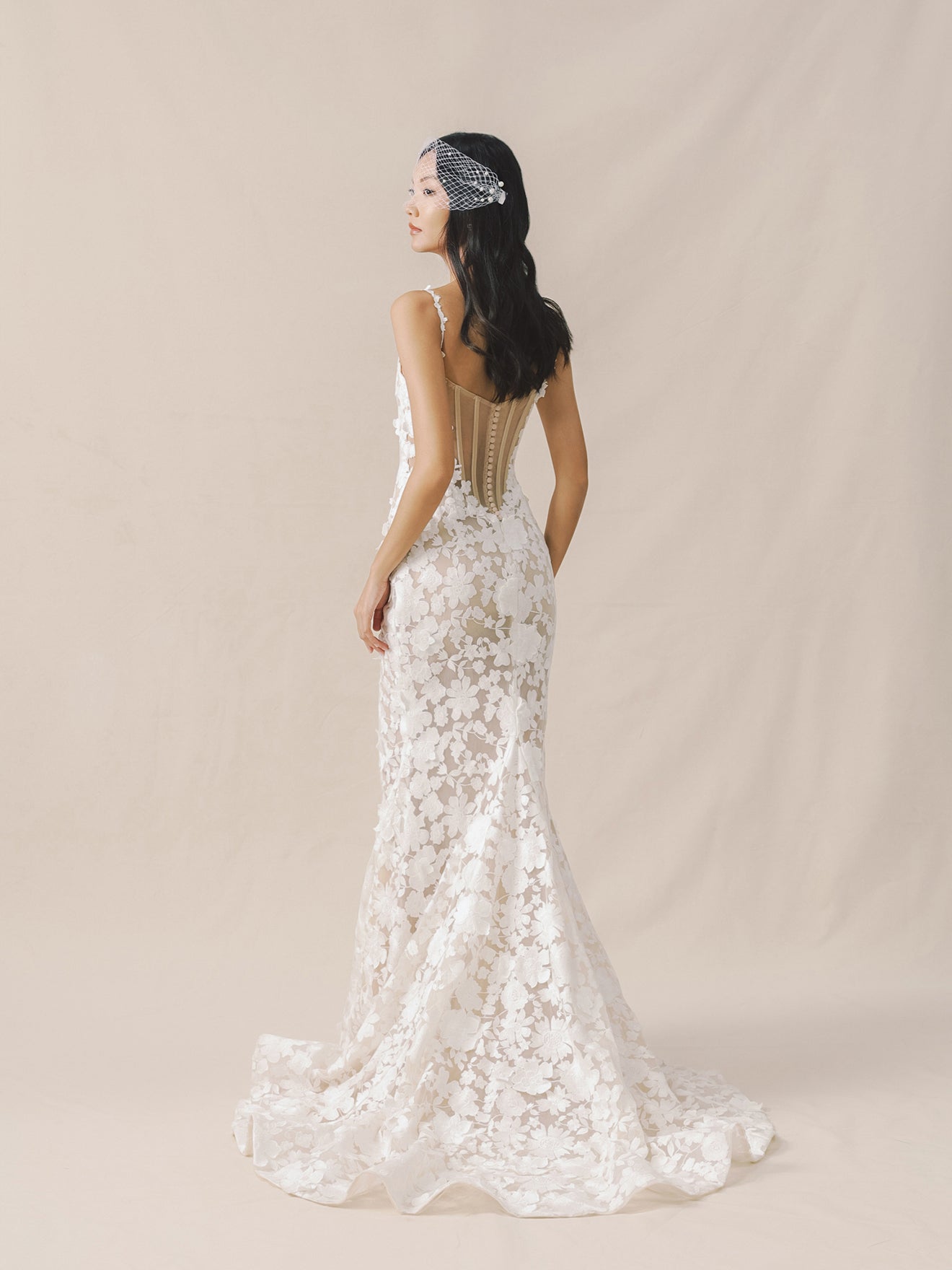 Woman wearing a white lace wedding dress with a beaded headband on a beige background