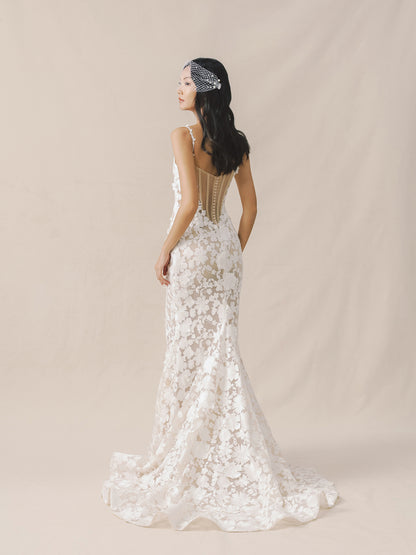 Woman wearing a white lace wedding dress with a beaded headband on a beige background