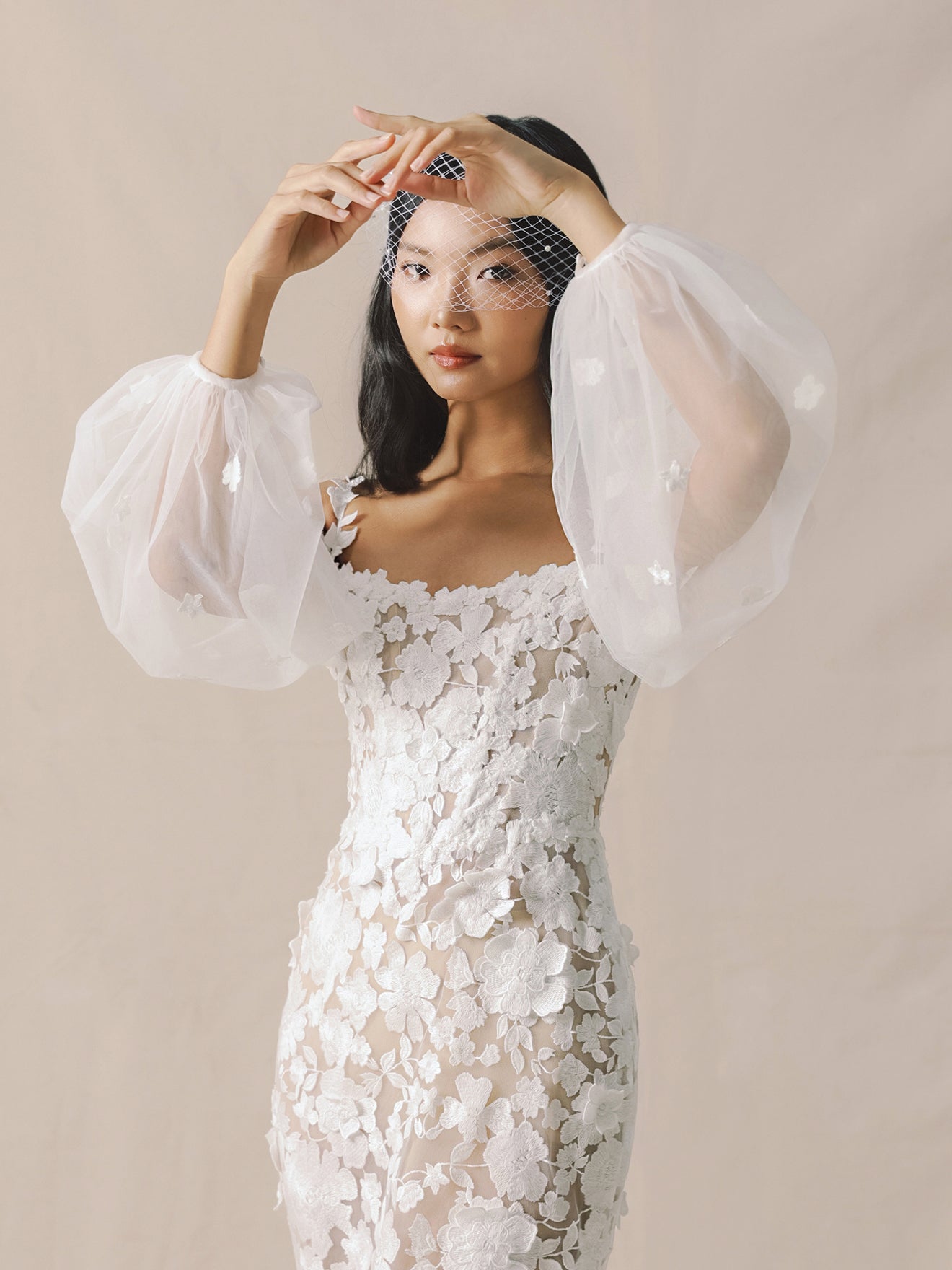 Woman wearing a white lace dress with sheer sleeves against a beige background