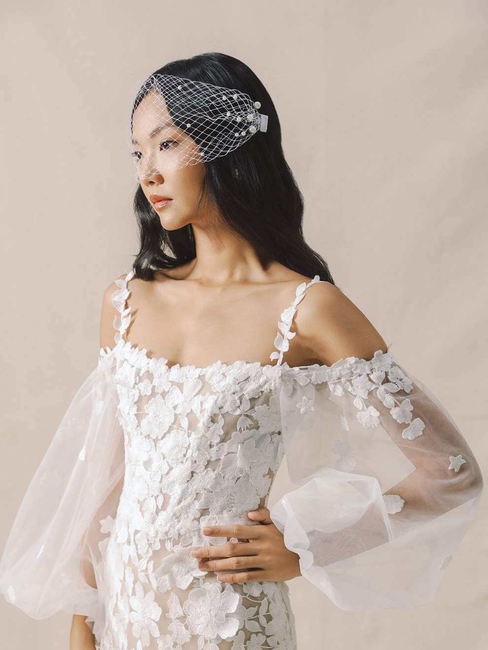 Woman wearing a white floral off-shoulder dress with sheer sleeves against a beige background