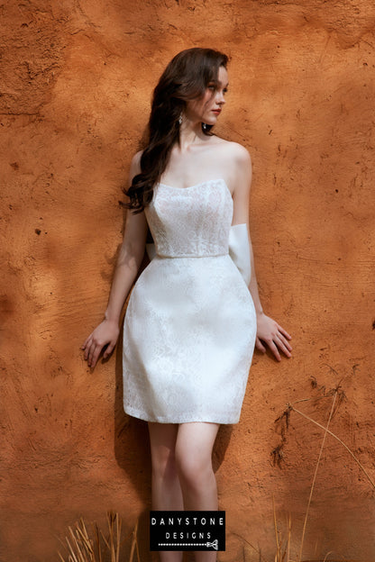 Model wearing the 2-in-1 lace strapless mini dress by Danystone Designs, standing against a rustic orange wall.