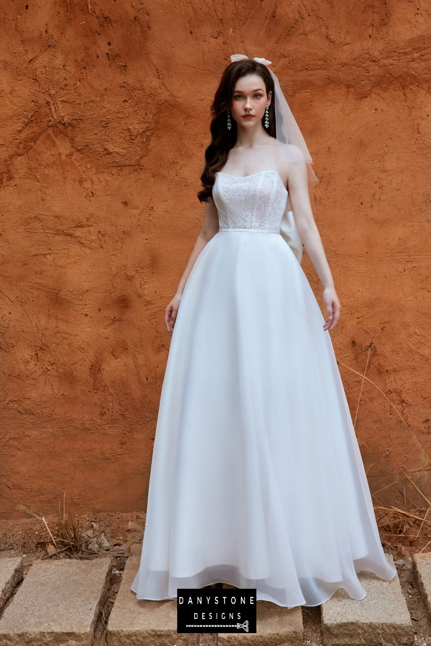 Model in a full-length wedding gown with a detachable silk chiffon skirt, lace bodice, and subtle bow detail, designed by Danystone Designs.