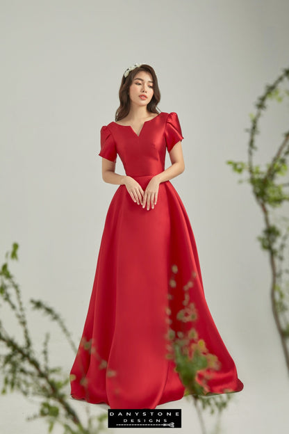 Woman wearing a red tafeta dress with fairy wing sleeves standing gracefully