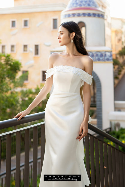 Image 3: Bride in a flat shoulder fishtail wedding dress with 3D floral accents, looking to the side on a balcony.