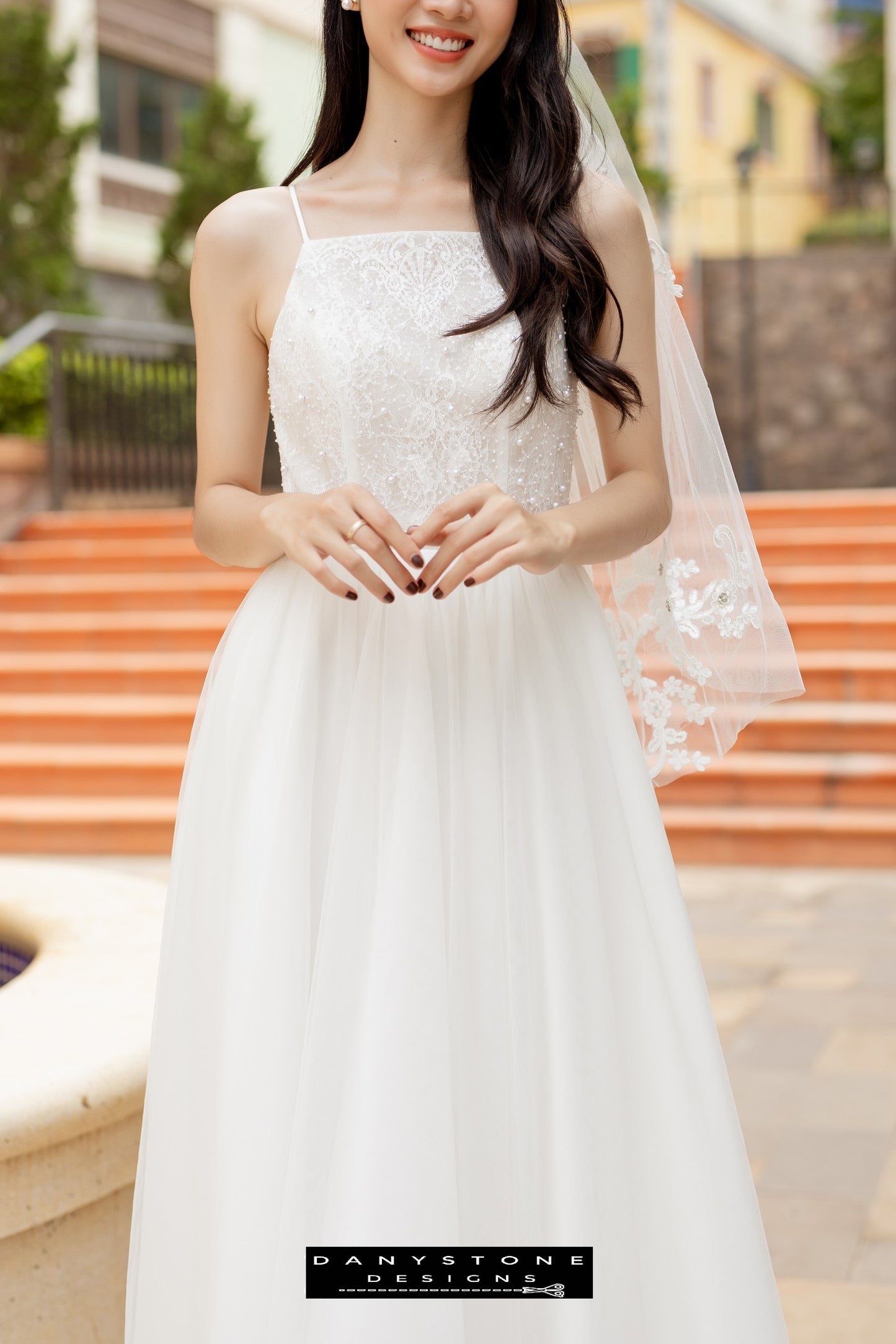 Image 4: Bride in a camisole wedding dress with mesh beads, posing on steps with hands clasped.