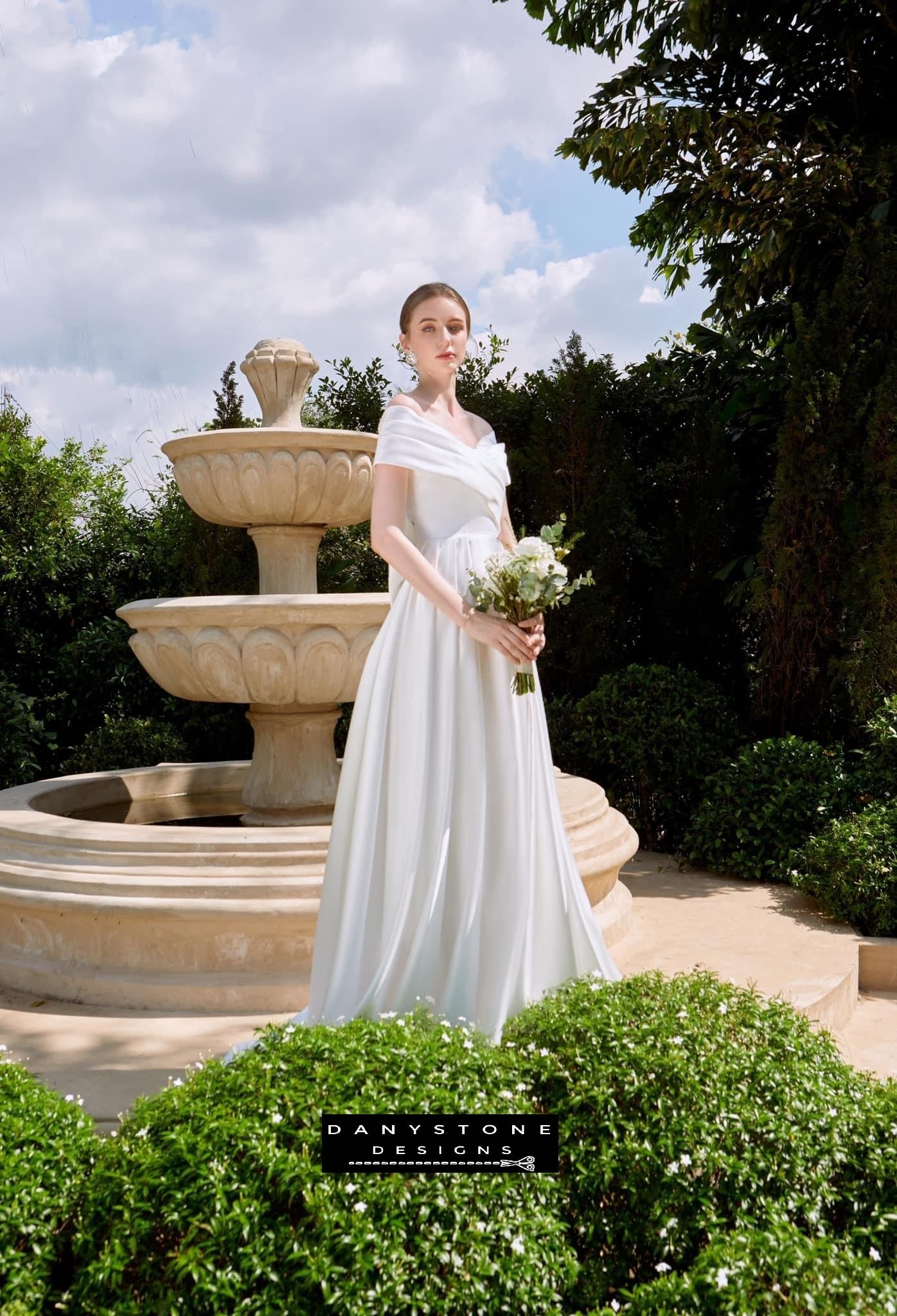 Elegant Bridal Gown with Pleated Bow - Side View - Model displaying the side view of the dress, highlighting the cross-breasted design and off-the-shoulder look.