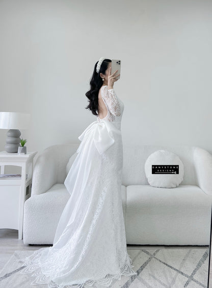 Bride in lace fishtail dress with full U back and silk chiffon bow, close-up front view.