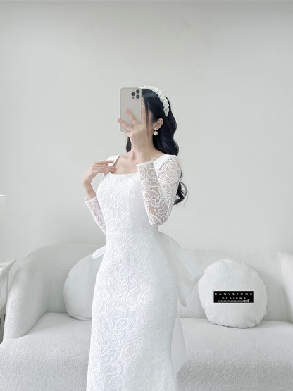 Bride in lace fishtail dress with full U back and silk chiffon bow, standing sideways.