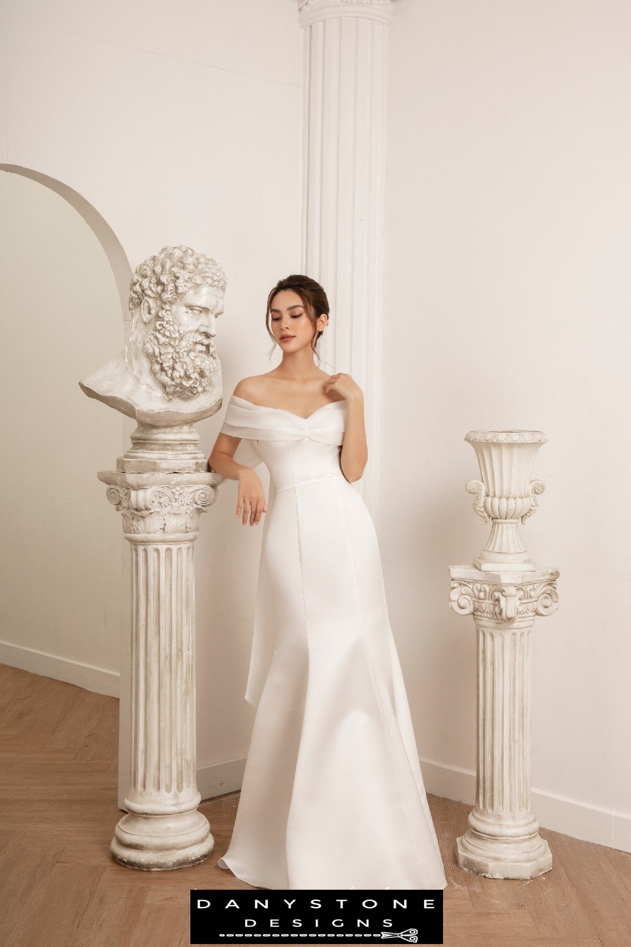 Bride in fishtail wedding dress with flat shoulders and silk chiffon trim, standing in elegant pose.