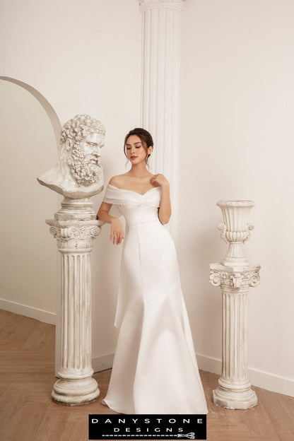 Bride in fishtail wedding dress with flat shoulders and silk chiffon trim, standing in elegant pose.