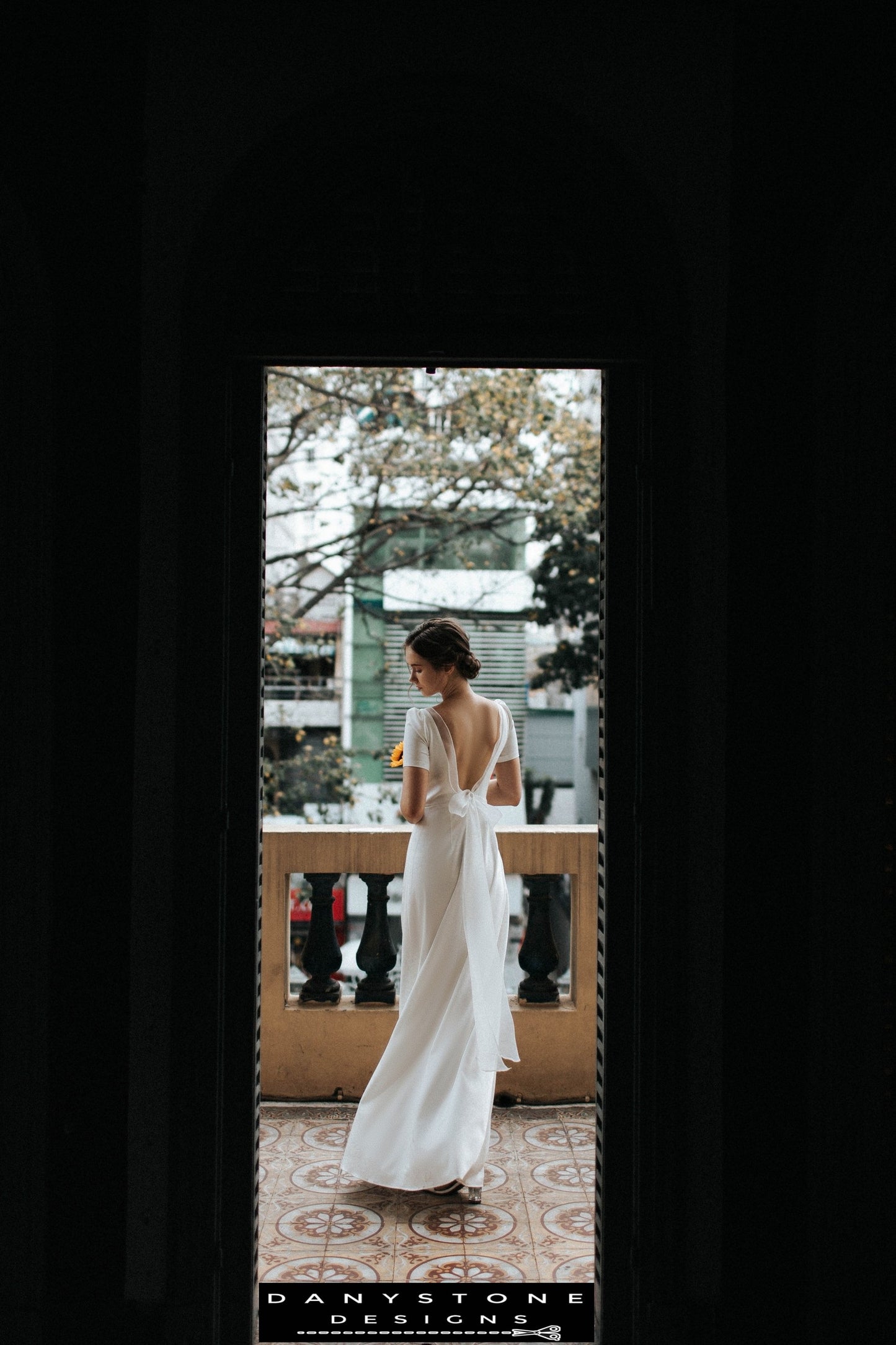 Elegant backless wedding dress with short sleeves and bow accent, holding sunflower – Danystone Designs