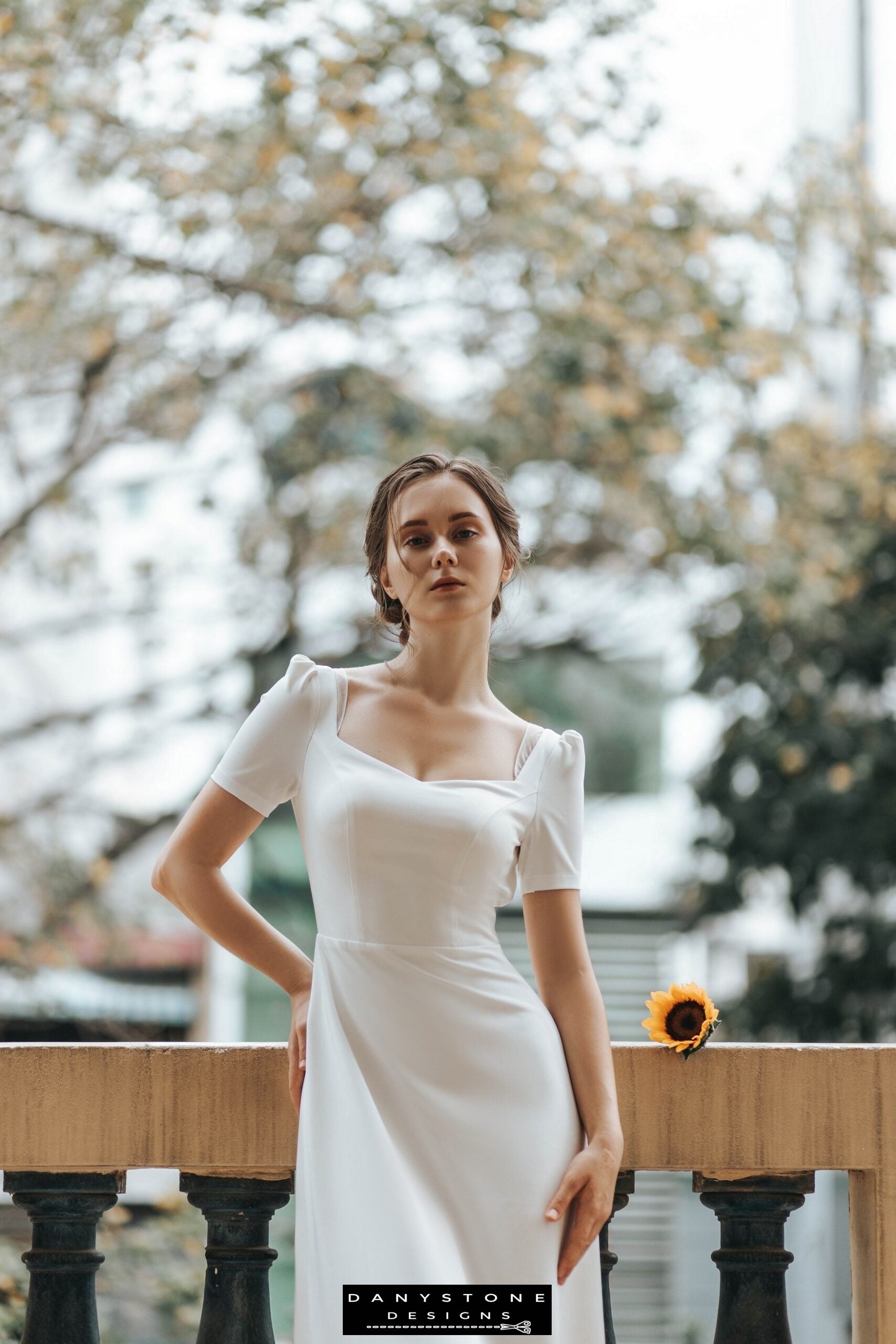 Bride in a backless wedding gown with bow detail, standing on a balcony – Danystone Designs