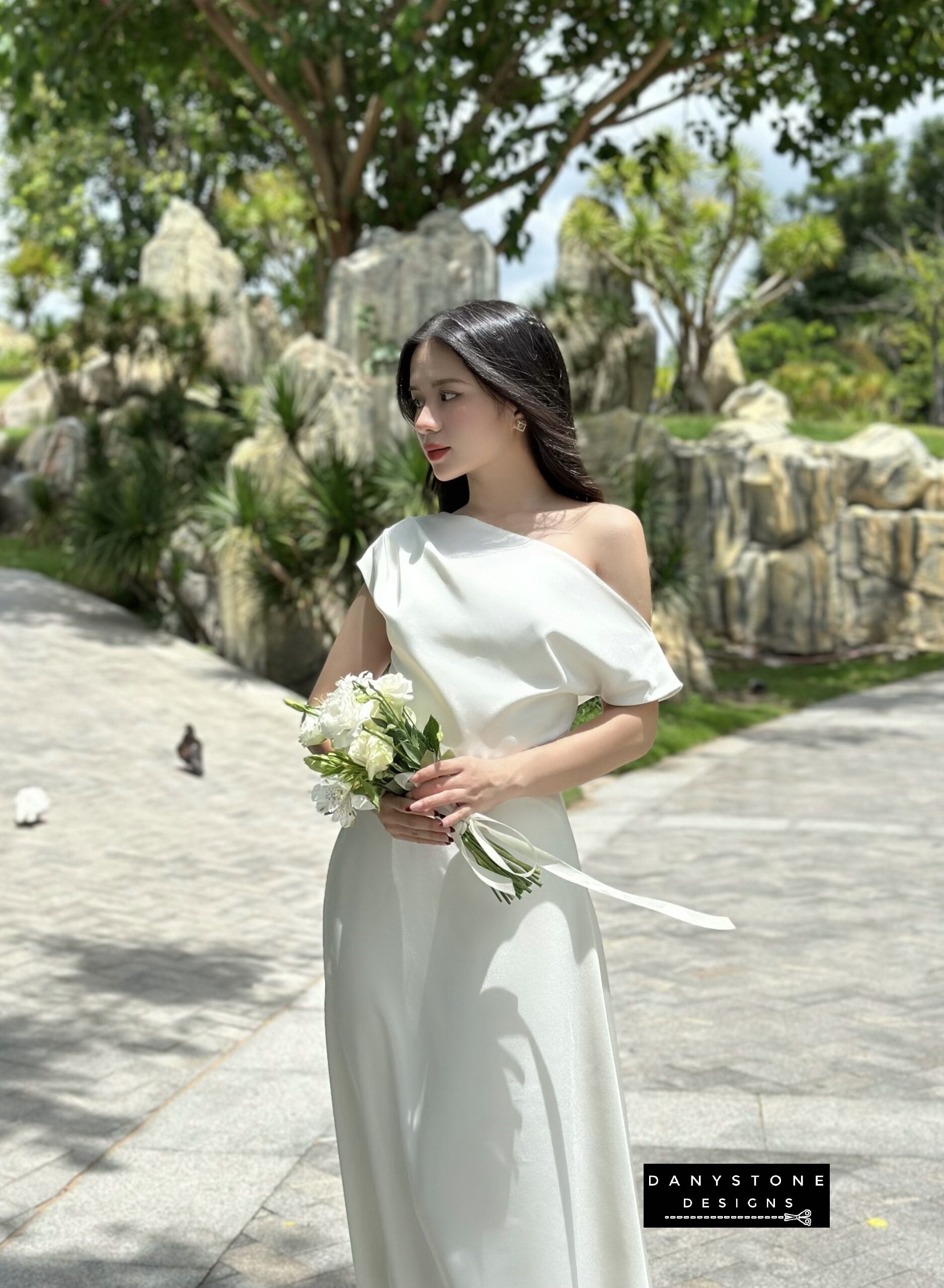 Model holding a bouquet in an off-the-shoulder satin wedding dress, front view.