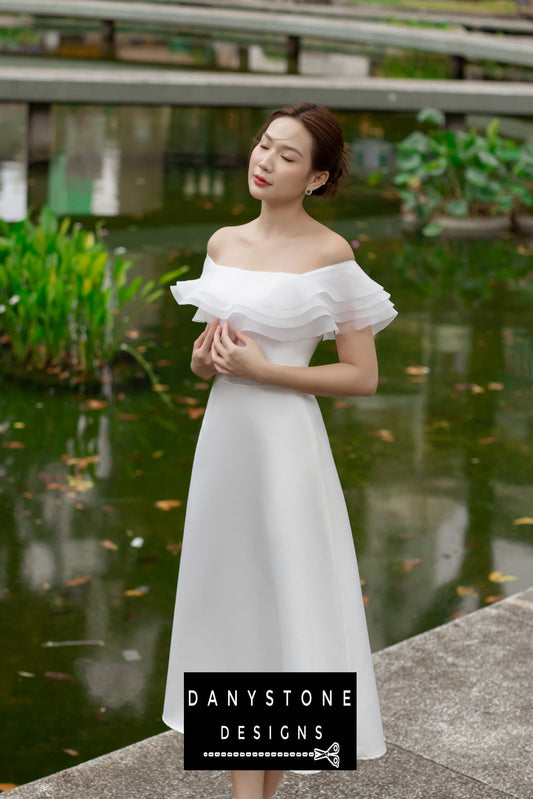 Woman in a white midi 4-layer flat-shoulder dress, standing by a serene pond.