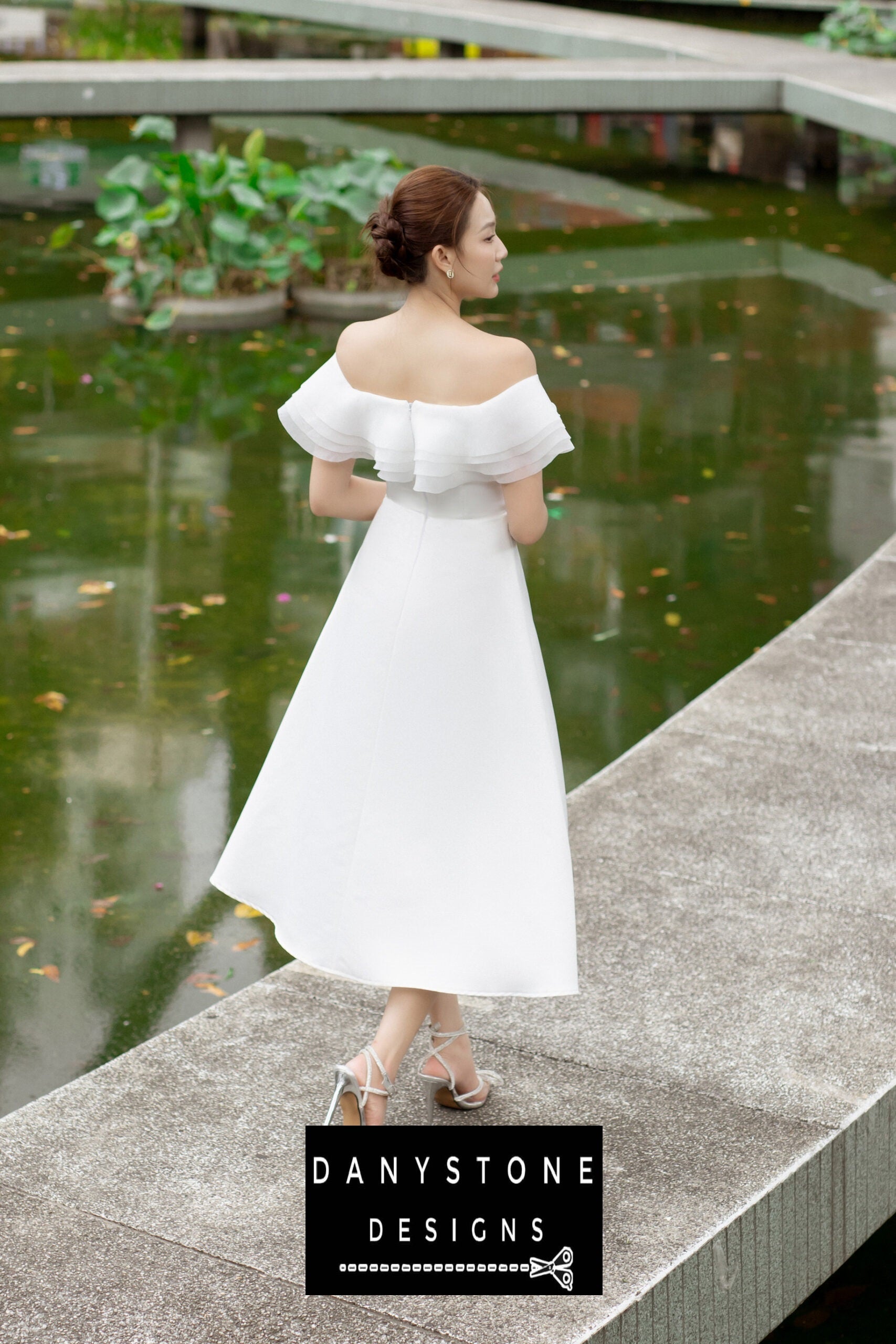 Back view of a woman wearing a white midi 4-layer flat-shoulder dress, showcasing the elegant layers.