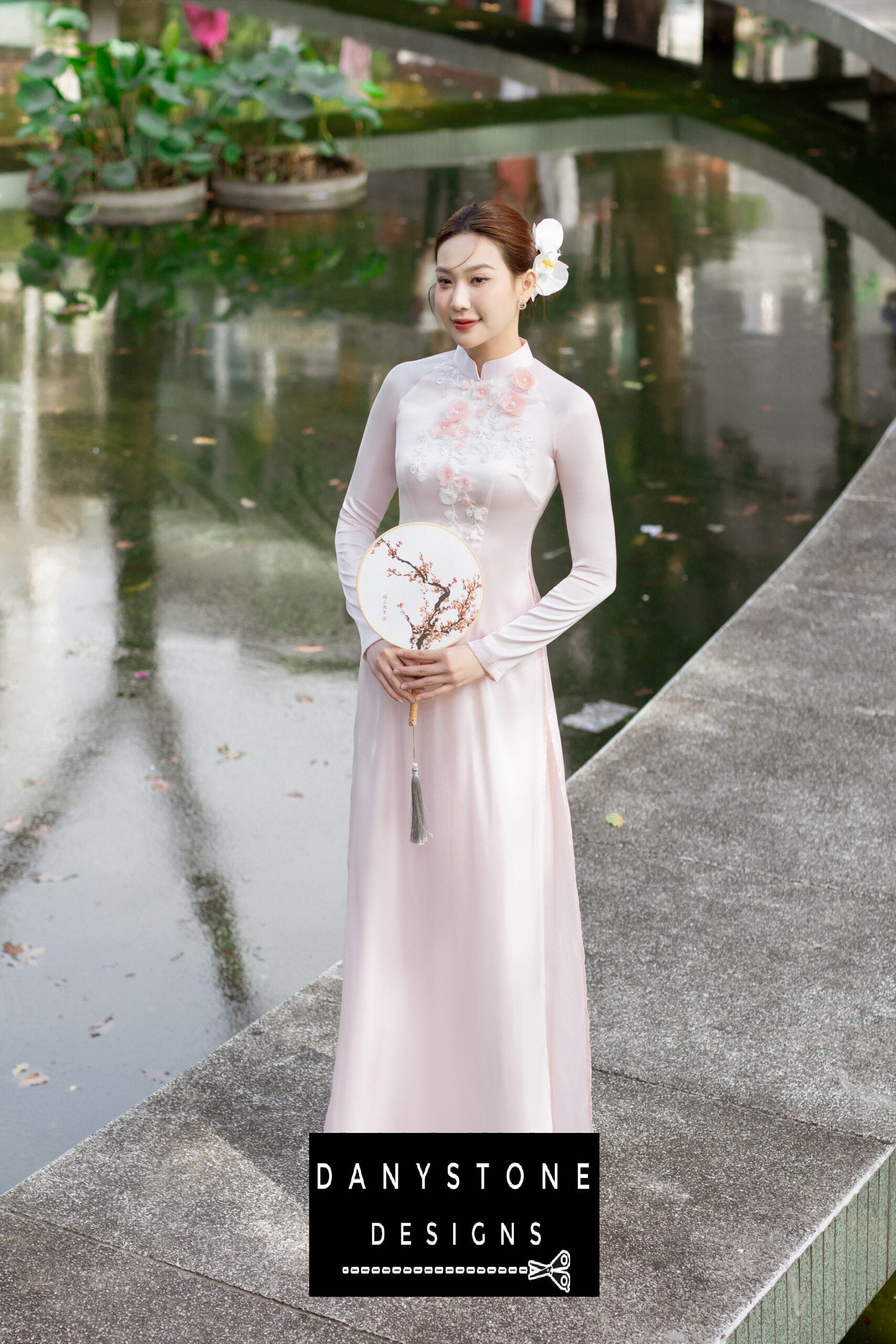 Side view of a woman wearing a pink silk chiffon Áo Dài, showcasing delicate floral details.