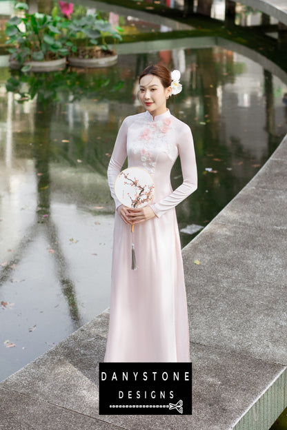 Side view of a woman wearing a pink silk chiffon Áo Dài, showcasing delicate floral details.