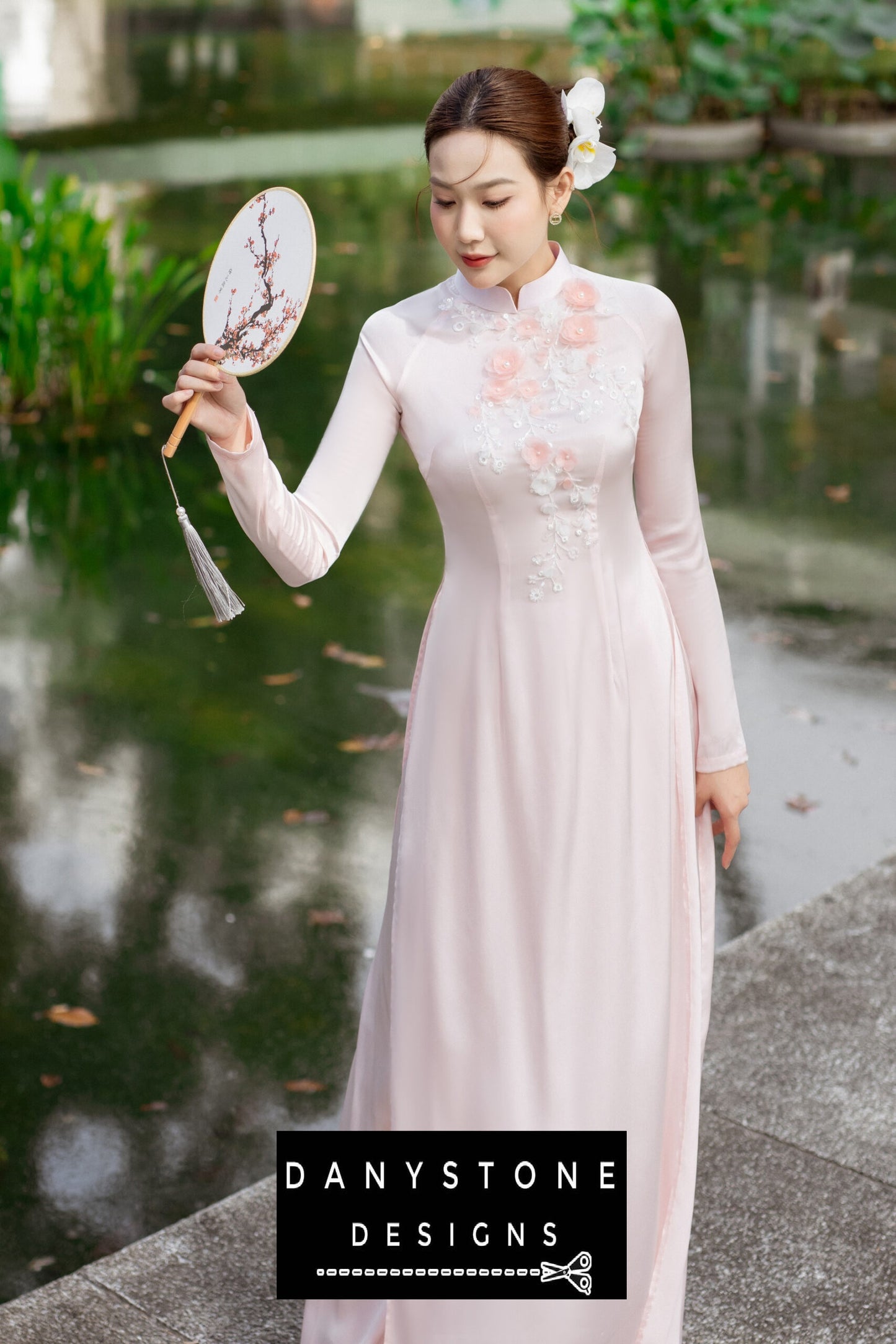 Close-up of floral embellishments on a pink silk chiffon Áo Dài, held by a woman.