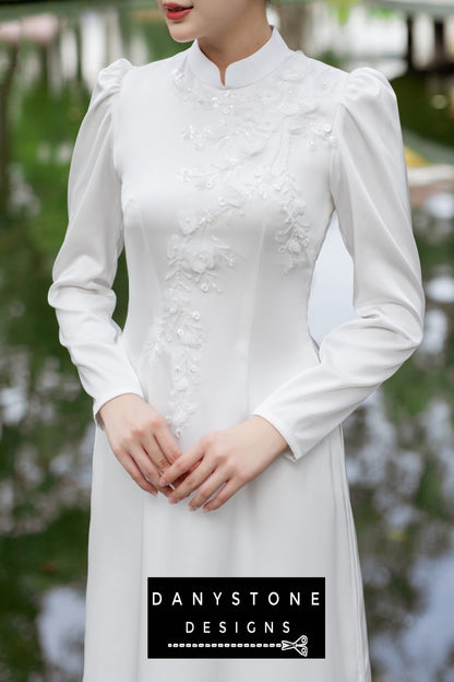 Close-up of a woman in a white silk chiffon Áo Dài with intricate floral embellishments.