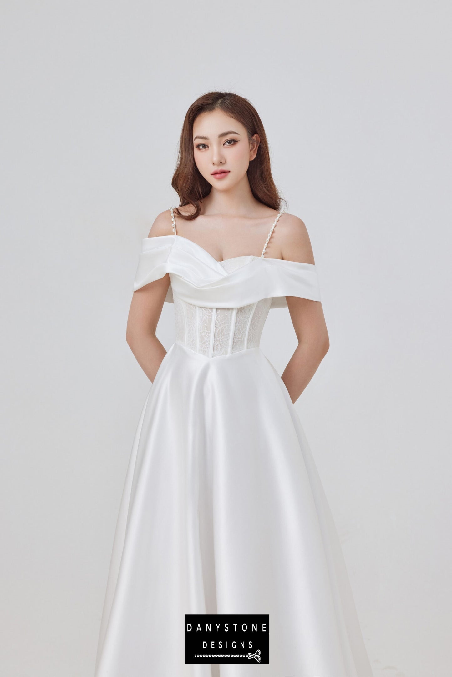 Elevate your bridal look with this exquisite satin off-shoulder wedding dress, showcasing a corset lace bodice and pearl straps. The flowing silhouette and luxurious satin fabric create a timeless and romantic look.